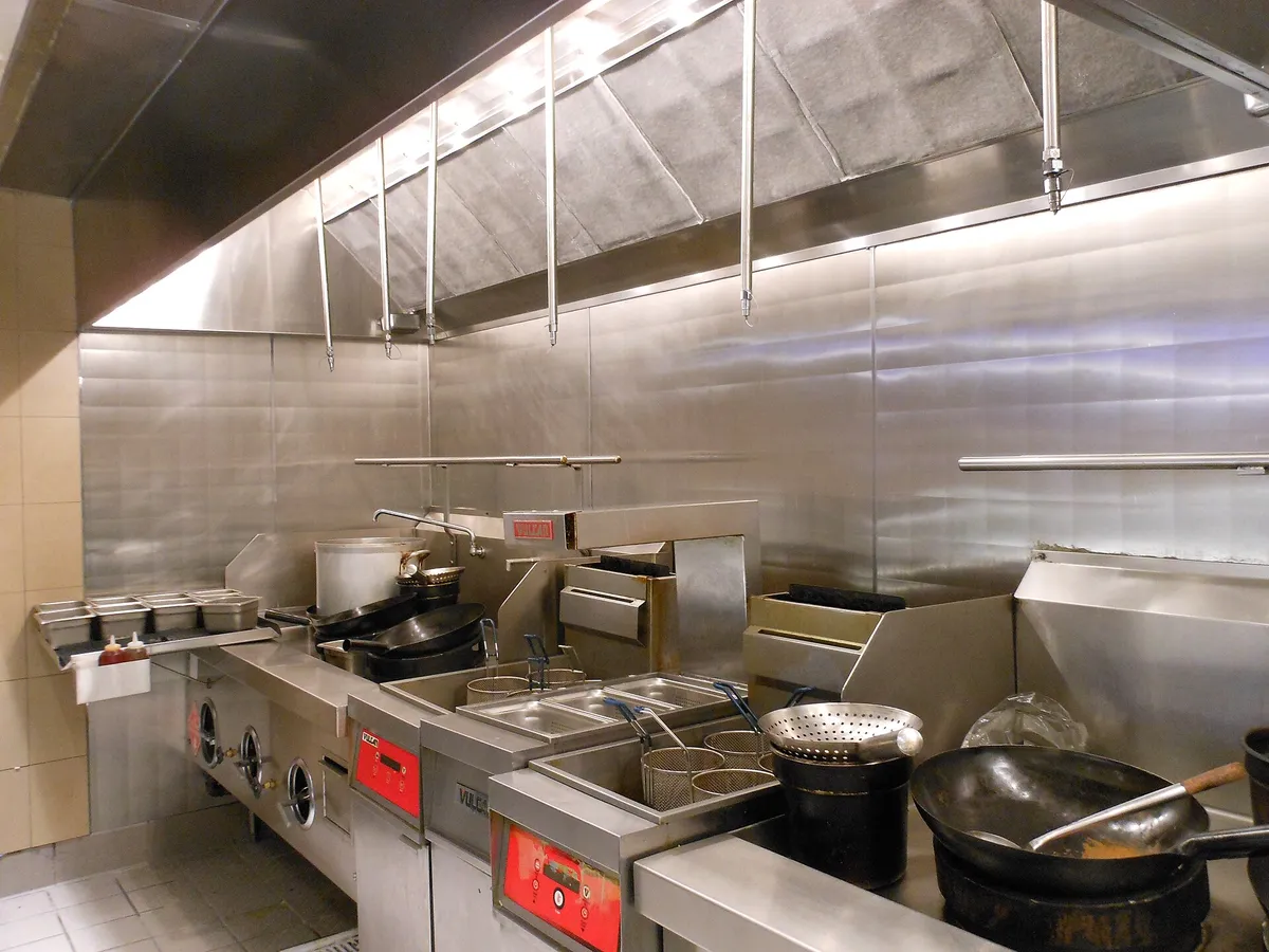 A stainless hood line over fryers and a range, where appliance positions are checked during a kitchen hood inspection