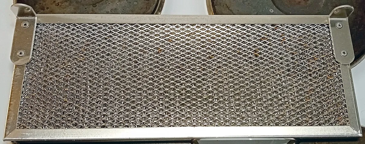 The same mesh hood filter after washing, with the bare metal visible again