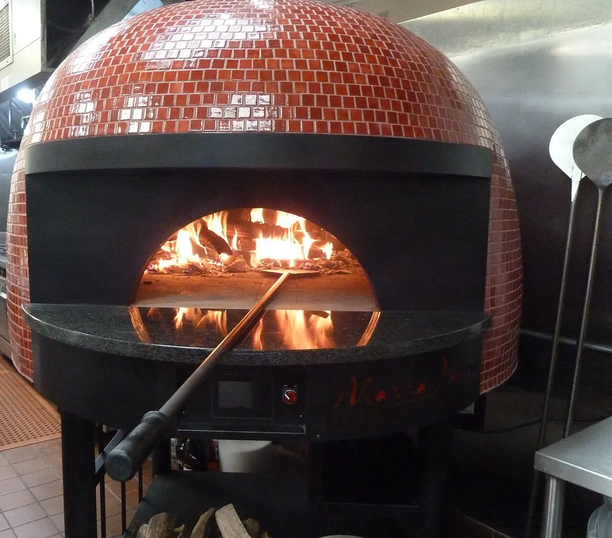 Wood-fired oven and smoker hood cleaning Huntsville AL example: a tiled wood-fired pizza oven with a live fire, the kind of solid fuel appliance on a monthly schedule